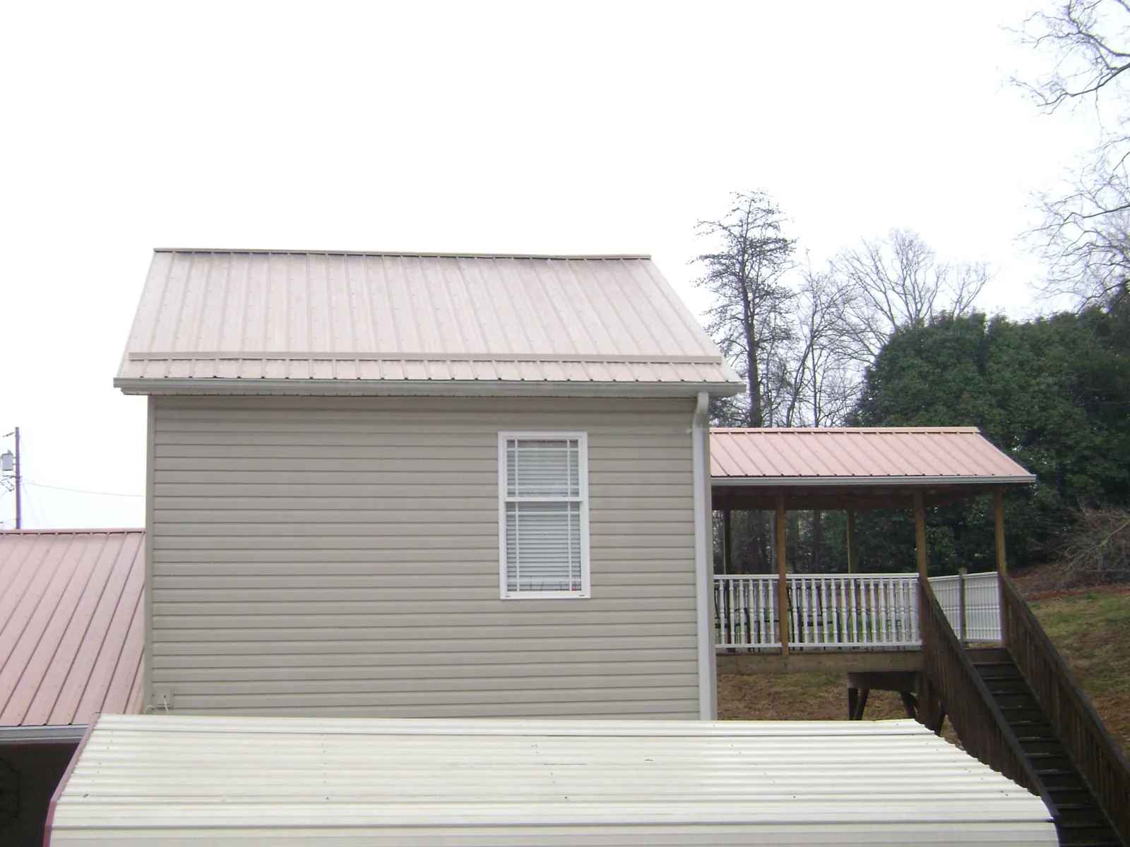 Tan metal roofs on a two story addition and attached porch, from a Roof Replacement job in Burnham